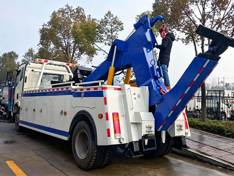 Blue white heavy‑duty wrecker tow truck with hydraulic lifting boom on parking lot