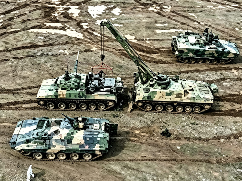 Camouflage armored recovery vehicle lifting equipment among military tanks on field terrain
