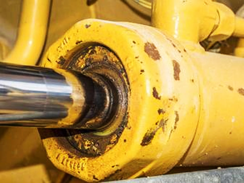 Close‑up view of worn leaking hydraulic cylinder rod seal on heavy equipment