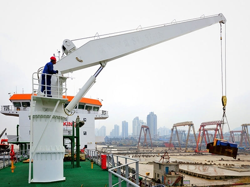 White marine hydraulic crane installed on ship deck, port shipyard background with worker operating