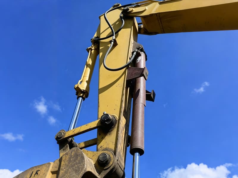 Yellow excavator hydraulic cylinders fitted on boom and dipper arm against blue sky