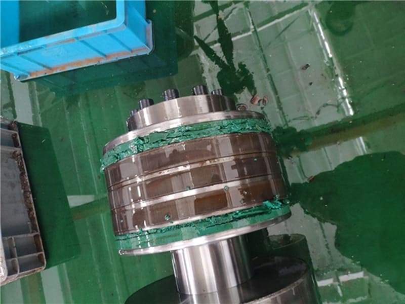 Disassembled multi‑stage hydraulic cylinder piston with damaged green sealing packing on workshop floor