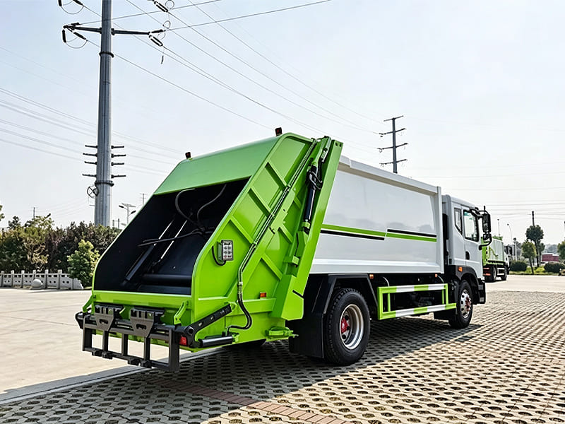 Green‑white refuse compactor truck showing rear hydraulic loading mechanism