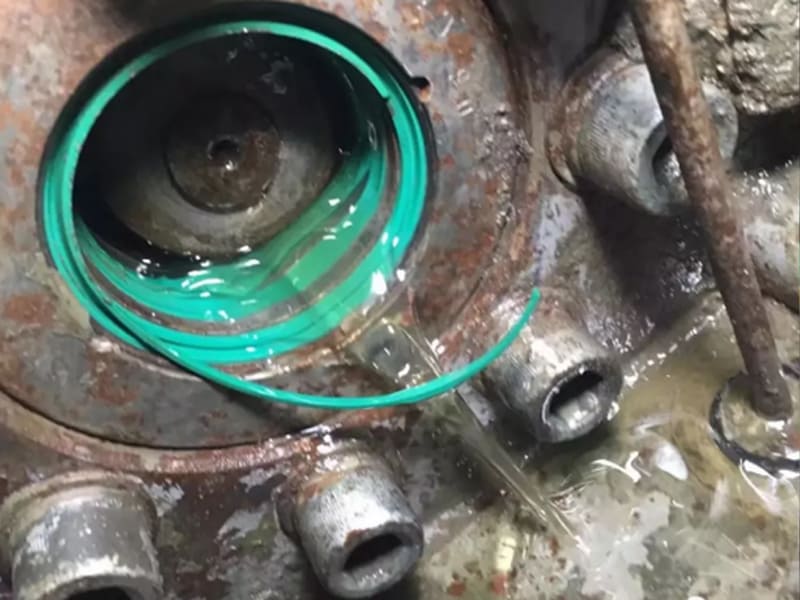 Broken green hydraulic seal causing oil leakage inside rusted cylinder housing