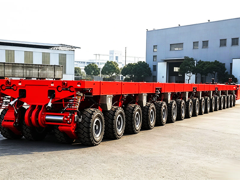 Red multi‑axle SPMT modular heavy‑duty trailer parked outside factory building
