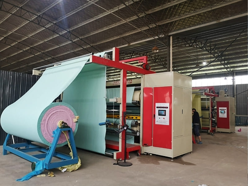 Large textile laminating machine processing big roll of non‑woven fabric in factory workshop