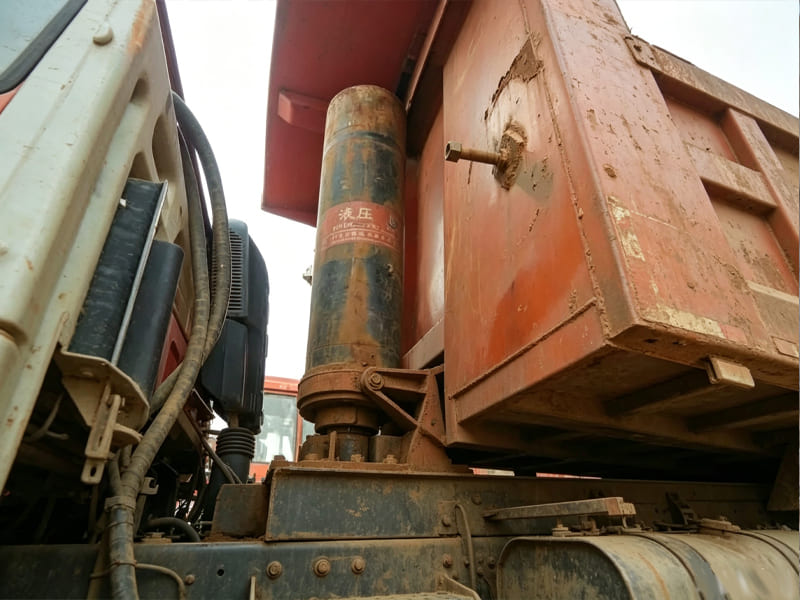Worn multi‑stage telescopic hydraulic cylinder installed on old mining dump truck