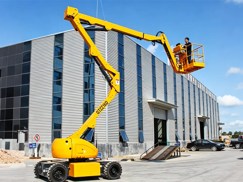 Yellow self‑propelled articulated aerial work platform outside modern factory building