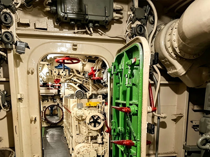 Interior view of ship engine room with complex hydraulic pipes, valves and mechanical assemblies