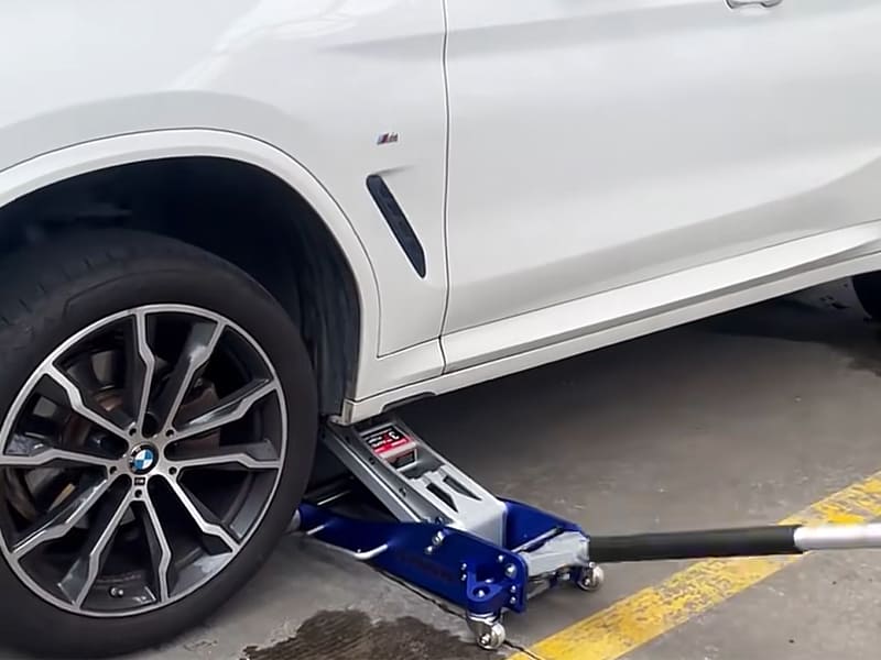 Blue low‑profile floor jack lifting SUV vehicle for tire repair