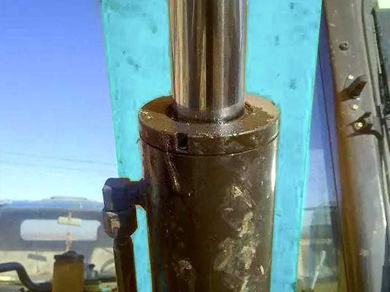Close-up shot of original excavator hydraulic cylinder outdoors, chrome piston rod and cylinder oil port detail