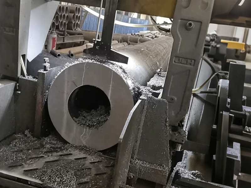 Industrial band saw machine cutting thick seamless hollow steel tube, metal chips scattered, factory raw material processing workshop