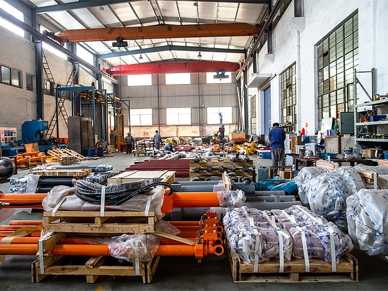 Factory workshop stocked with finished hydraulic cylinders packed on wooden pallets, overhead crane inside workshop