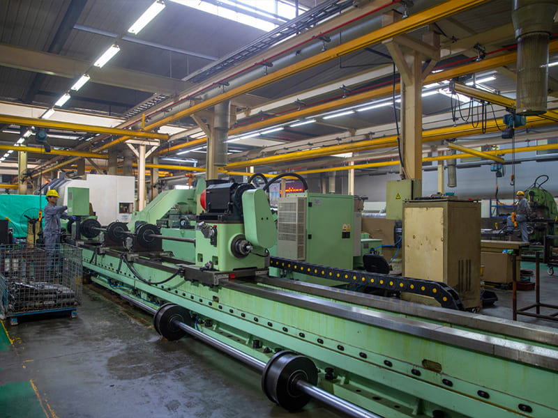 Large long lathe machine processing hydraulic piston rods inside factory workshop