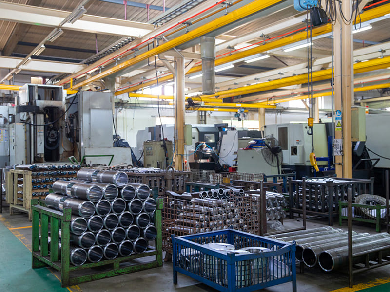 Stacked machined hydraulic cylinder tubes stored in racks inside machining workshop