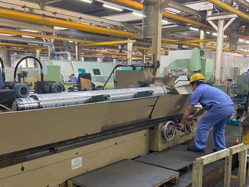 Worker operates grinding machine to polish the surface of hydraulic cylinder piston rod