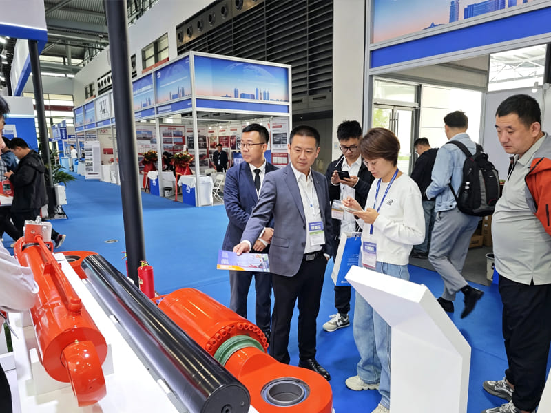 Exhibition booth displaying heavy hydraulic cylinders, sales staff introduce products to visiting customers