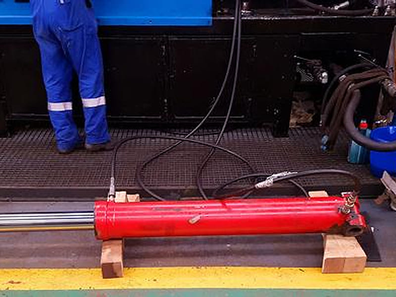 Red large bore hydraulic cylinder on pressure test bench in workshop