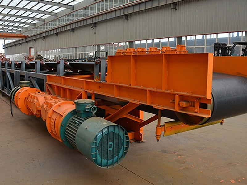 Large orange heavy‑duty belt conveyor with drive motor inside factory workshop