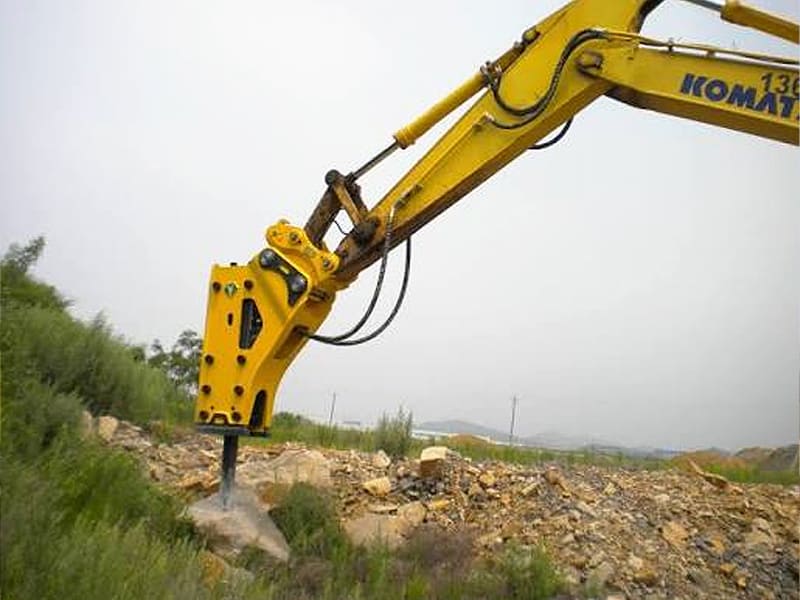 Yellow Komatsu excavator with hydraulic hammer breaking rocks on site