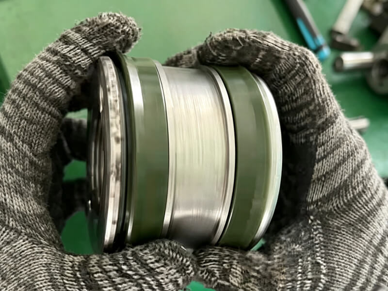 Gloved hands holding hydraulic piston unit with combined sealing rings for forklift cylinder