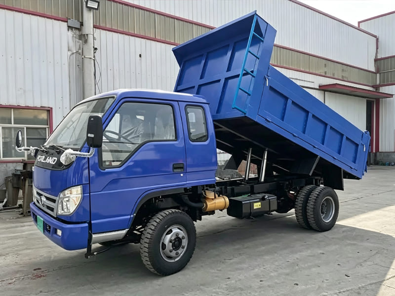 Small blue light‑duty dump truck with lifted cargo box in factory yard