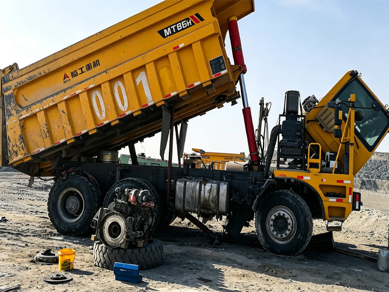 Yellow mining dump truck MT86H, cargo box lifted, mine site maintenance scene
