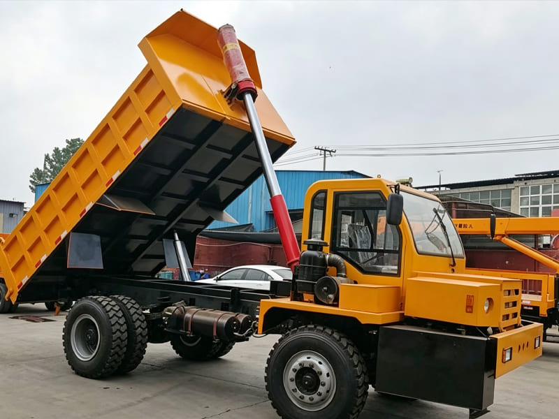 Yellow off‑road dump truck, cargo box lifted by multi‑stage hydraulic cylinder, factory yard scene