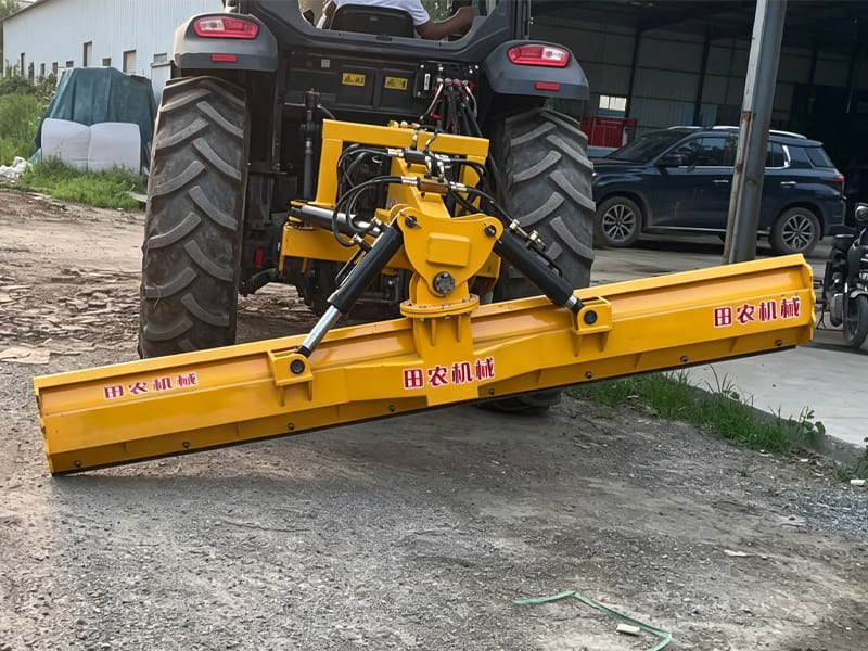 Yellow hydraulic land grader attached to rear of farm tractor