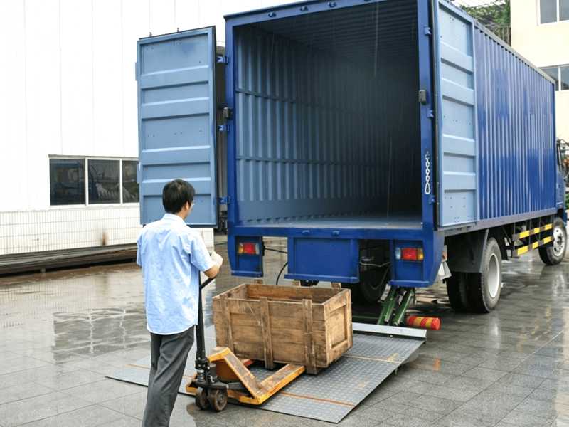 Worker uses hand pallet truck to load wooden crate via blue box truck hydraulic tail lift