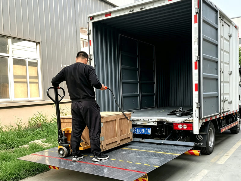 Worker pushing wooden crate onto truck using hydraulic tail lift platform