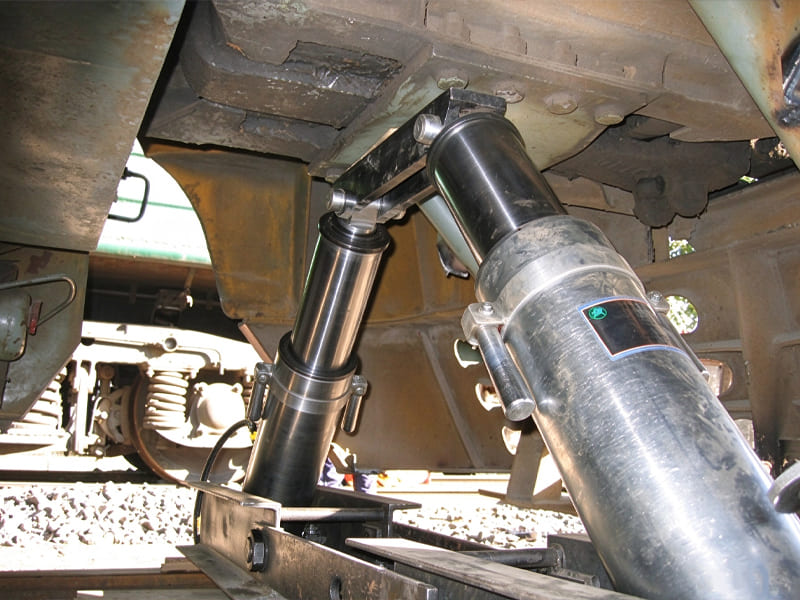 Two heavy-duty hydraulic cylinders under train chassis, used for railway vehicle rerailing and recovery work