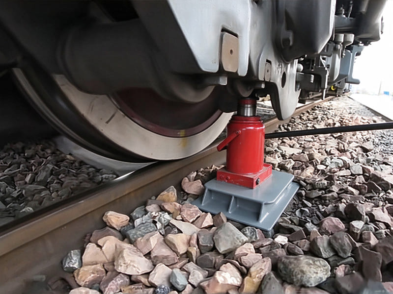 Red portable hydraulic jack placed on ballast track, lifting railway wheel set for on-site maintenance