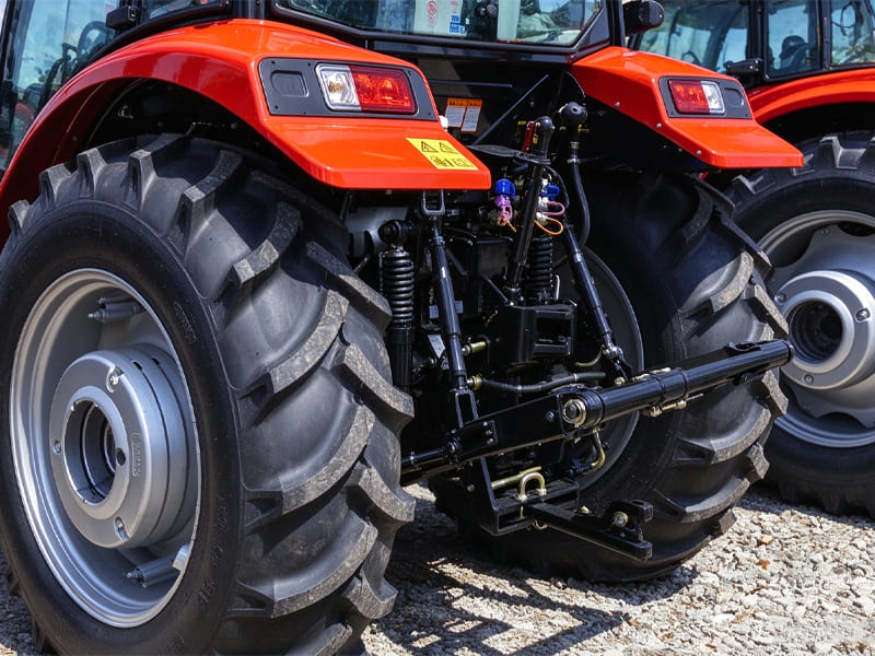 Rear view of red farm tractor, showing three-point hitch and hydraulic connection system, agricultural tractor parked on gravel ground