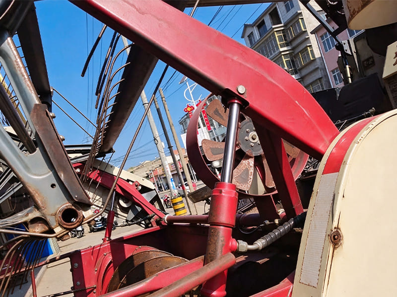 Close-up field shot of red combine harvester header lifting hydraulic cylinder, installed on farm harvesting machine under blue sky