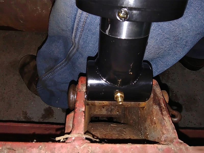 Black multi-stage telescopic hydraulic cylinder mounted on agricultural equipment frame, field installation site