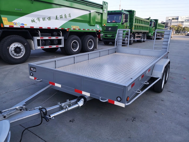 Grey twin axle flatbed utility trailer with loading ramps, diamond plate cargo floor, no hydraulic tipping function