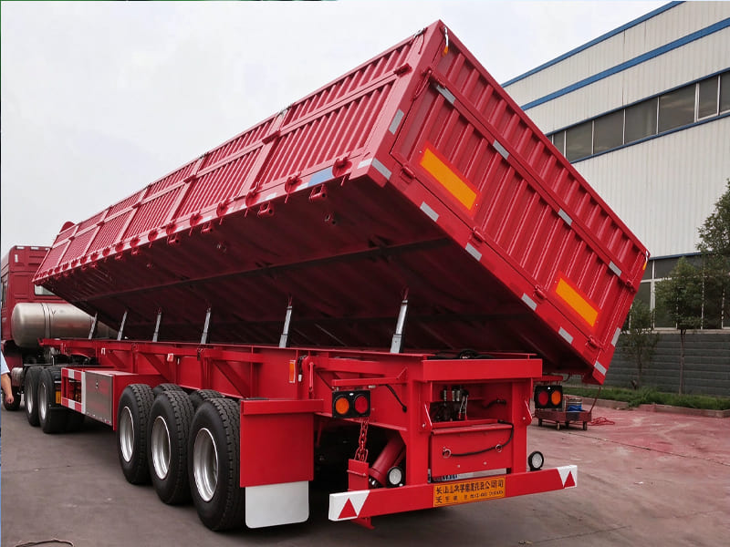 Red side tipping semi-trailer, multiple hydraulic cylinders lifting cargo body, heavy transport side dump trailer