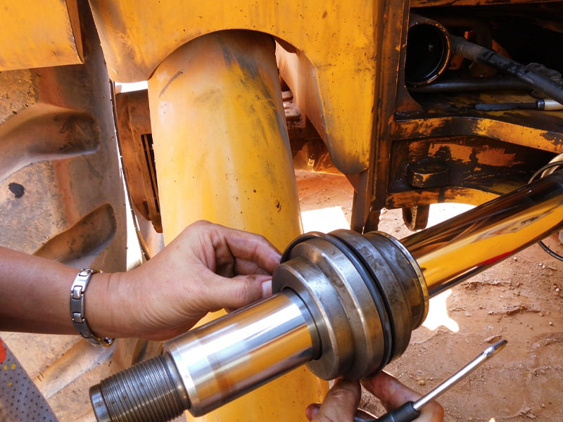 Technician installing sealing kits on hydraulic cylinder piston rod, on-site repair of construction machinery cylinder