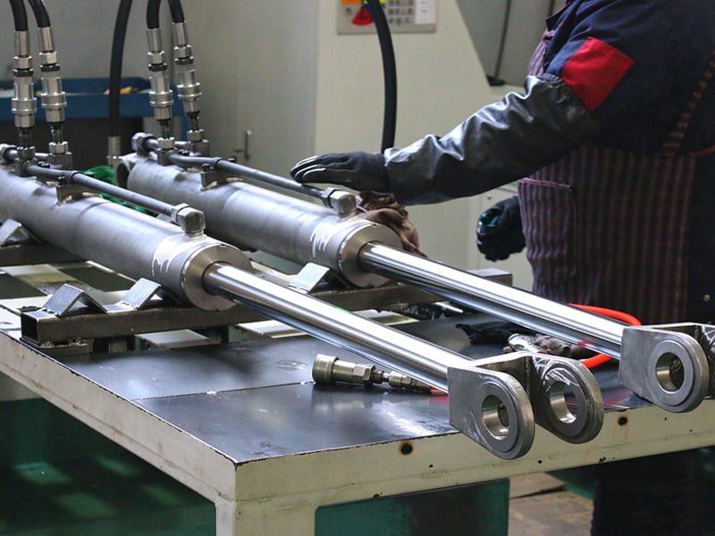 Factory worker assembling heavy duty tie rod hydraulic cylinders with rod eyes, finished hydraulic cylinders on workbench