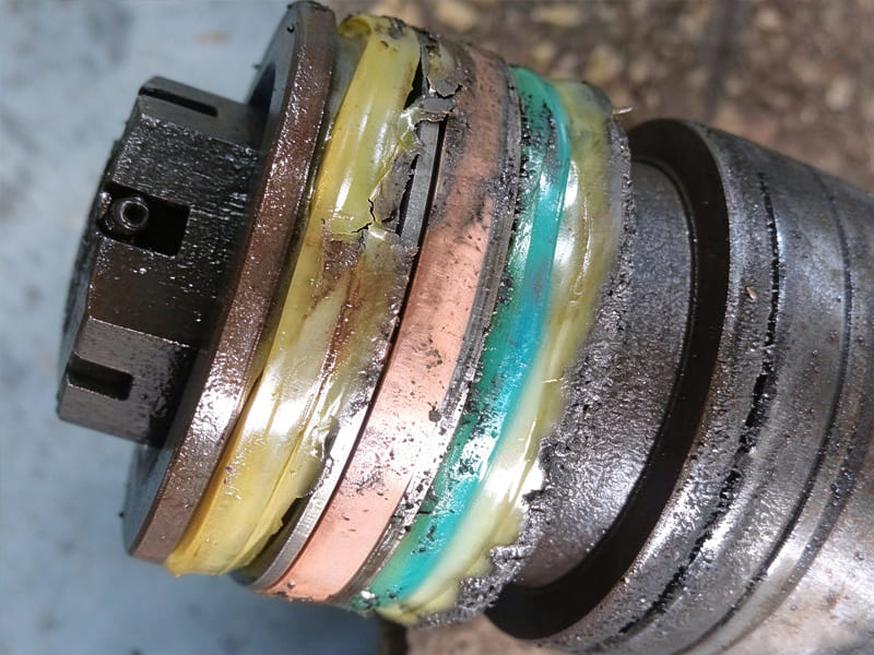 Disassembled hydraulic cylinder showing worn and damaged piston seal stack