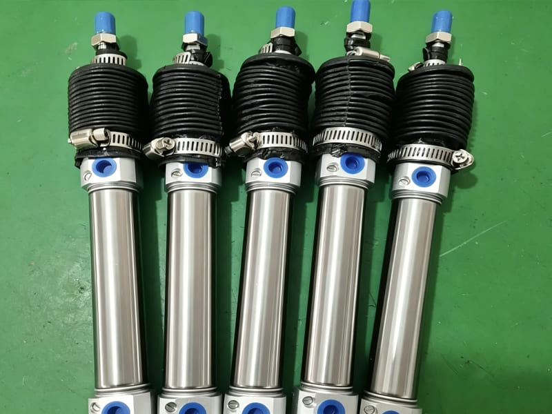 Group of stainless steel mini air cylinders equipped with rubber dust boots on green workbench